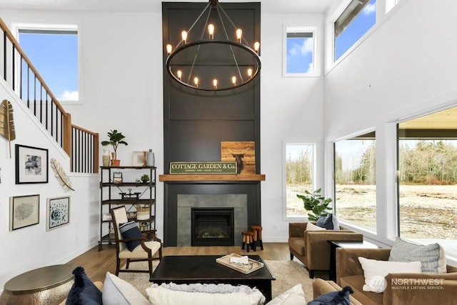 living room with a towering ceiling, a tiled fireplace, light hardwood / wood-style flooring, and a notable chandelier