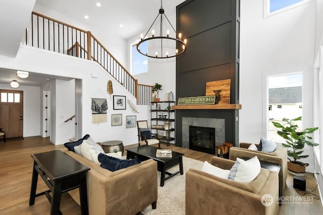 living room with a high ceiling, a tile fireplace, hardwood / wood-style floors, and an inviting chandelier