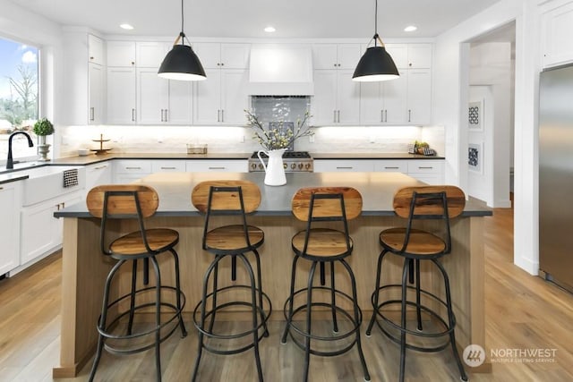 kitchen with wall chimney exhaust hood, hanging light fixtures, a kitchen island, and white cabinets