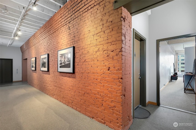 hallway featuring rail lighting, brick wall, a towering ceiling, and carpet