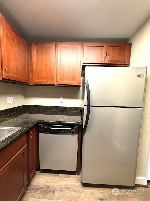 kitchen with appliances with stainless steel finishes, sink, light hardwood / wood-style floors, and dark stone counters