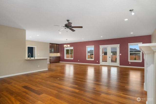 unfurnished living room with sink, ceiling fan with notable chandelier, and dark hardwood / wood-style floors