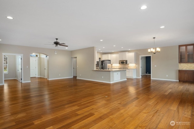 unfurnished living room featuring ceiling fan with notable chandelier and hardwood / wood-style floors