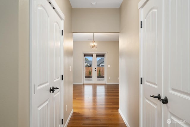 hallway featuring hardwood / wood-style flooring, french doors, and a notable chandelier