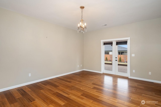 spare room featuring an inviting chandelier, hardwood / wood-style floors, and french doors