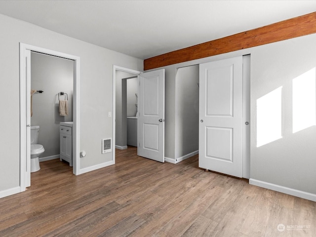 unfurnished bedroom featuring hardwood / wood-style floors, ensuite bath, and a closet