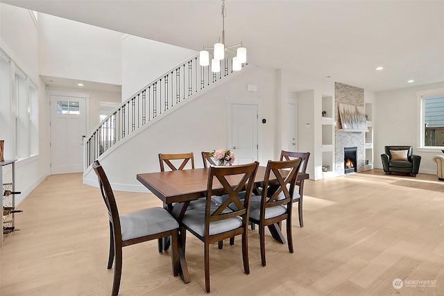 dining area featuring a tiled fireplace, stairway, light wood-type flooring, and an inviting chandelier