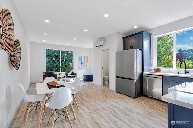 kitchen with sink, blue cabinetry, appliances with stainless steel finishes, a wall mounted air conditioner, and light hardwood / wood-style floors