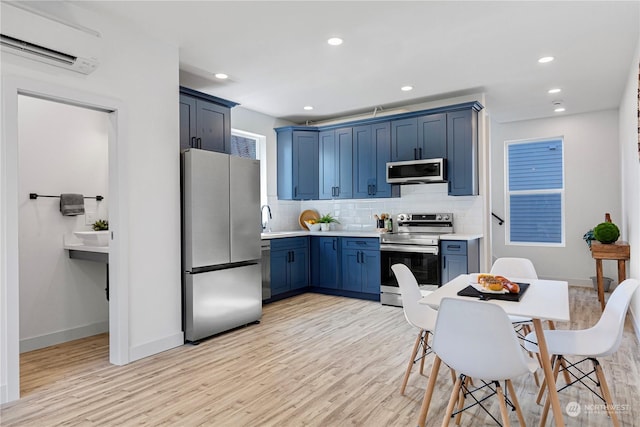 kitchen with blue cabinetry, stainless steel appliances, a wall mounted air conditioner, and light hardwood / wood-style flooring