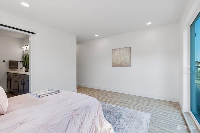 bedroom featuring connected bathroom, a barn door, and light hardwood / wood-style flooring