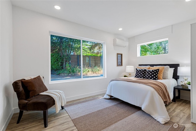 bedroom featuring light wood-type flooring, multiple windows, and an AC wall unit