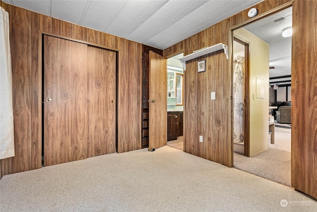 unfurnished bedroom featuring light carpet, a textured ceiling, wooden walls, and a closet