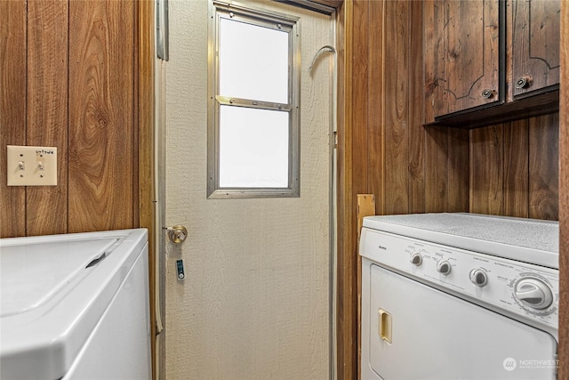 laundry area featuring cabinets, washing machine and dryer, and wooden walls