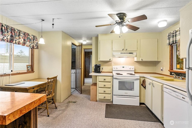 kitchen featuring sink, white appliances, hanging light fixtures, light carpet, and washer / dryer