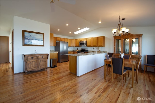 kitchen with hanging light fixtures, stainless steel appliances, light stone counters, vaulted ceiling, and light wood-type flooring