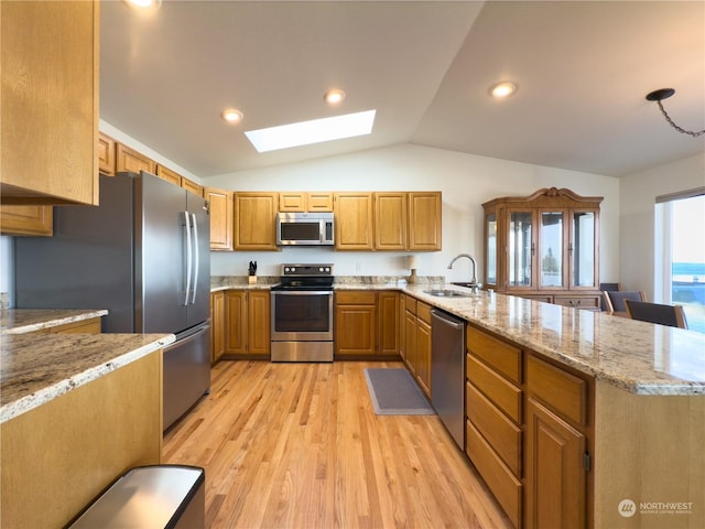 kitchen with appliances with stainless steel finishes, sink, light stone counters, kitchen peninsula, and light wood-type flooring