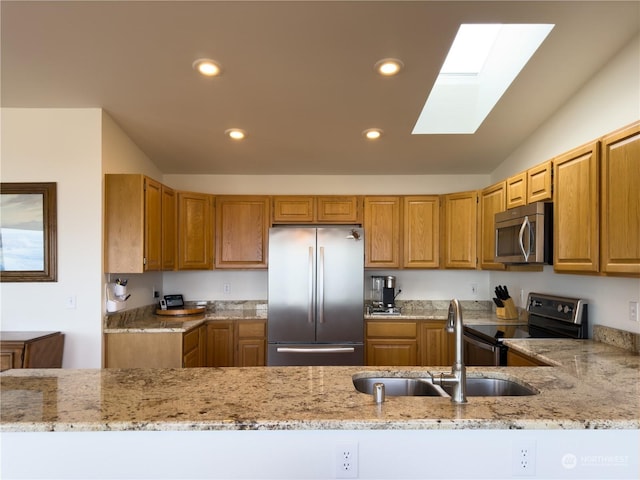 kitchen featuring light stone counters, appliances with stainless steel finishes, vaulted ceiling with skylight, and sink