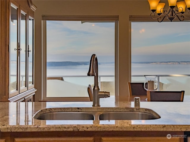 kitchen with sink, light stone countertops, a chandelier, and a water view