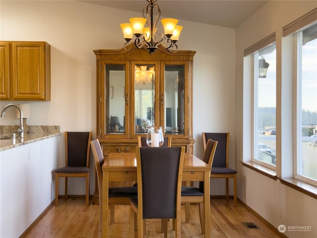 dining space with a healthy amount of sunlight, sink, light hardwood / wood-style flooring, and a notable chandelier