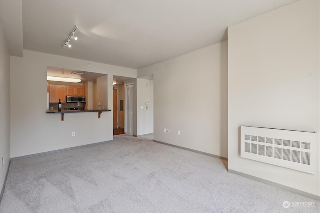 unfurnished living room featuring light carpet, radiator heating unit, and rail lighting