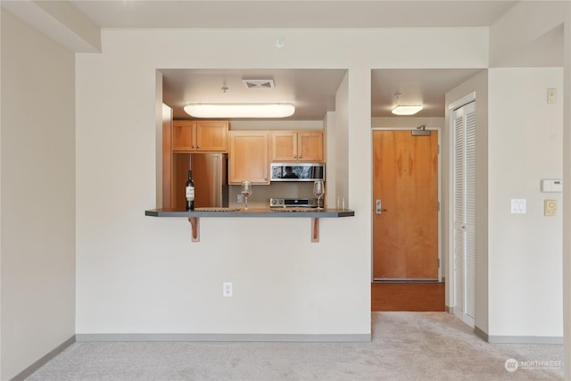 kitchen featuring light brown cabinetry, a breakfast bar area, kitchen peninsula, light colored carpet, and stainless steel appliances