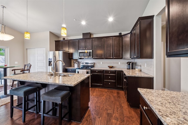 kitchen featuring sink, light stone counters, hanging light fixtures, stainless steel appliances, and a kitchen island with sink