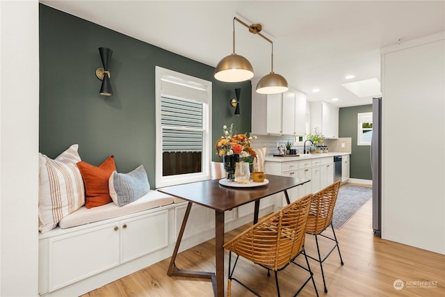 kitchen featuring sink, white cabinetry, light hardwood / wood-style flooring, pendant lighting, and decorative backsplash