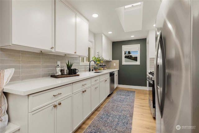 kitchen with stainless steel appliances, tasteful backsplash, white cabinets, and light hardwood / wood-style floors