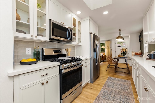 kitchen with backsplash, stainless steel appliances, white cabinets, decorative light fixtures, and light wood-type flooring