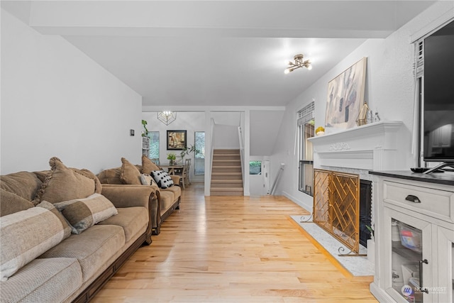 living room with a notable chandelier, a healthy amount of sunlight, a high end fireplace, and light wood-type flooring