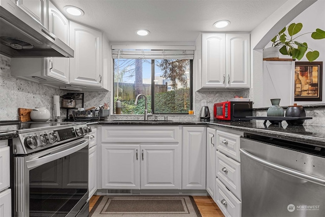 kitchen with appliances with stainless steel finishes, sink, white cabinets, and wall chimney exhaust hood