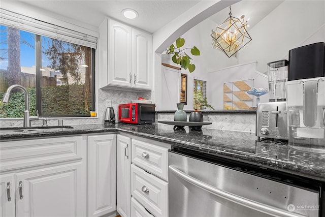 kitchen featuring sink, white cabinetry, stainless steel dishwasher, pendant lighting, and dark stone counters