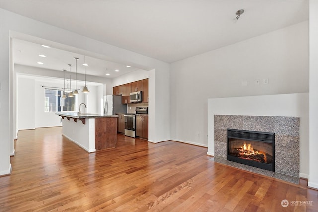 kitchen featuring a kitchen bar, hanging light fixtures, a center island with sink, light wood-type flooring, and stainless steel appliances