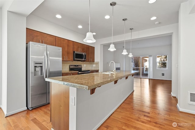 kitchen featuring a kitchen bar, sink, hanging light fixtures, stainless steel appliances, and a kitchen island with sink