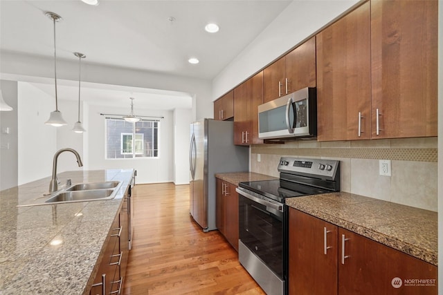 kitchen featuring appliances with stainless steel finishes, pendant lighting, sink, decorative backsplash, and light hardwood / wood-style floors