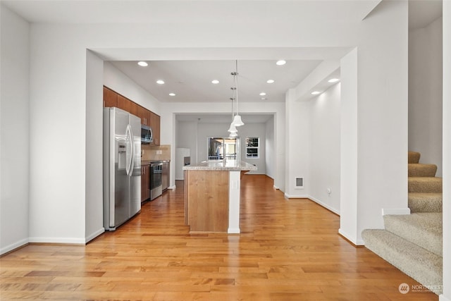 kitchen with light stone counters, hanging light fixtures, stainless steel appliances, light hardwood / wood-style floors, and backsplash