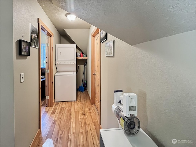 laundry area with stacked washer / dryer, a textured ceiling, and light hardwood / wood-style flooring