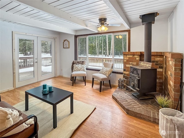 sunroom / solarium with a wood stove, ceiling fan, wooden ceiling, beam ceiling, and french doors