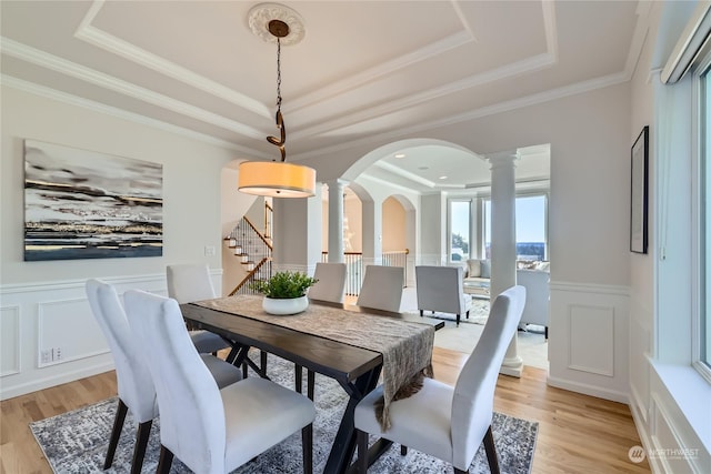 dining space featuring crown molding, a tray ceiling, light hardwood / wood-style floors, and decorative columns