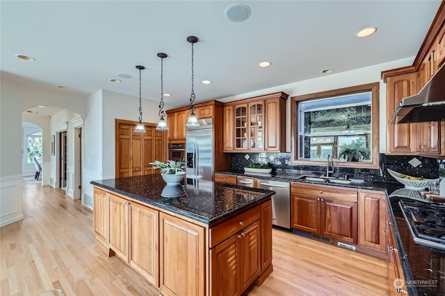 kitchen with sink, dark stone countertops, stainless steel appliances, a kitchen island, and decorative light fixtures