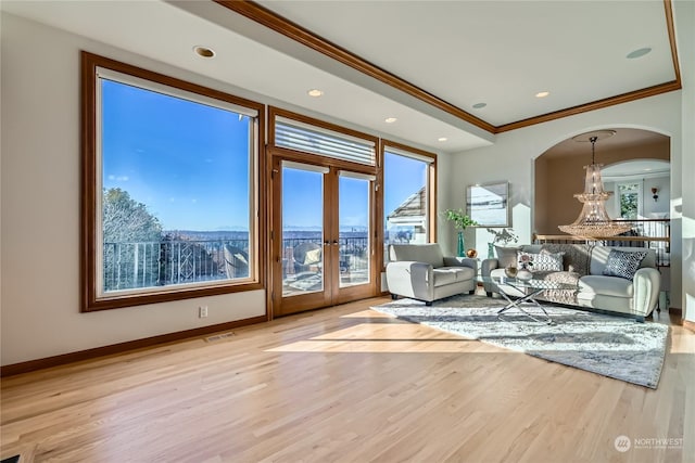 unfurnished living room with french doors, crown molding, a chandelier, and light wood-type flooring