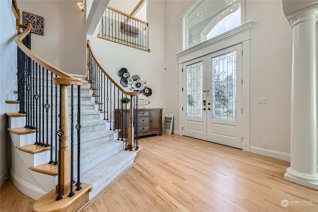 foyer entrance featuring a towering ceiling, decorative columns, french doors, and light wood-type flooring