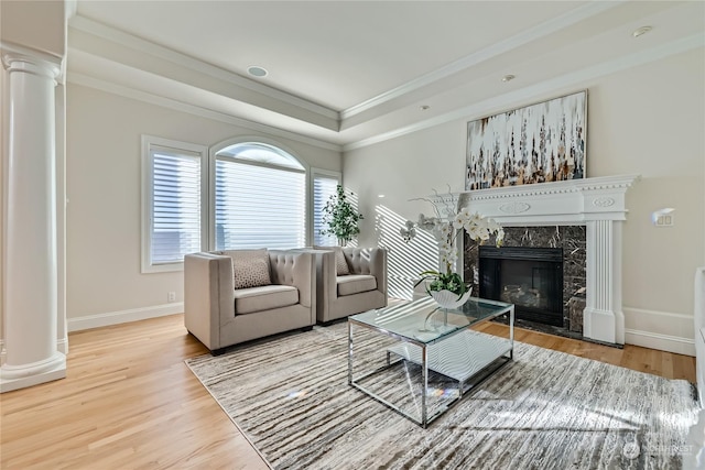 living room with crown molding, hardwood / wood-style flooring, decorative columns, a high end fireplace, and a raised ceiling