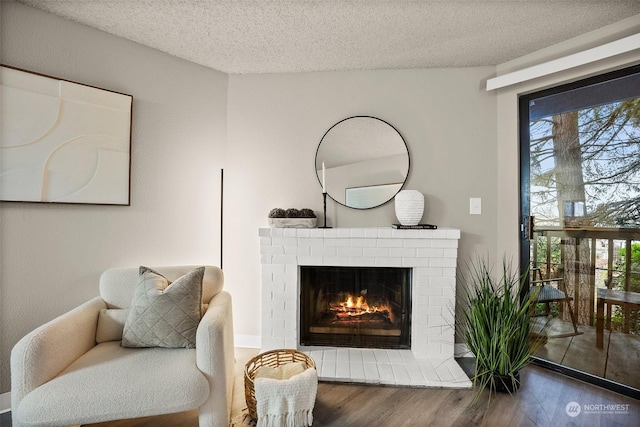 sitting room featuring plenty of natural light, a brick fireplace, wood-type flooring, and a textured ceiling