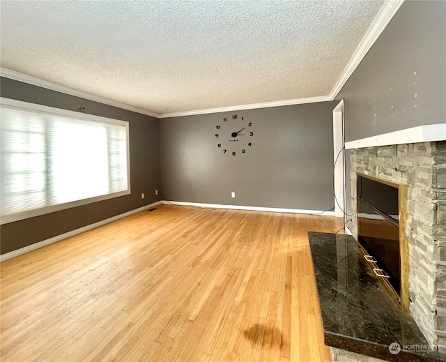 unfurnished living room with hardwood / wood-style flooring, a textured ceiling, a stone fireplace, and ornamental molding