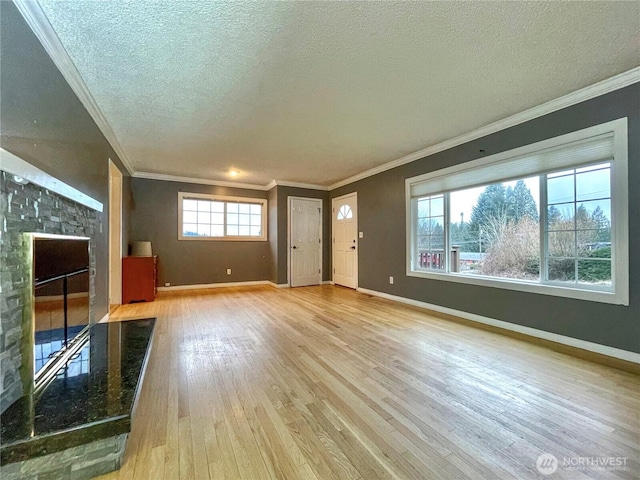 unfurnished living room featuring ornamental molding, light hardwood / wood-style floors, a textured ceiling, and a stone fireplace