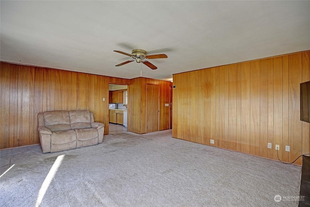 unfurnished living room with ceiling fan, light colored carpet, and wood walls