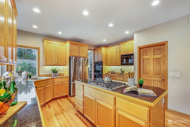 kitchen with sink, a center island, light brown cabinets, light hardwood / wood-style floors, and black appliances