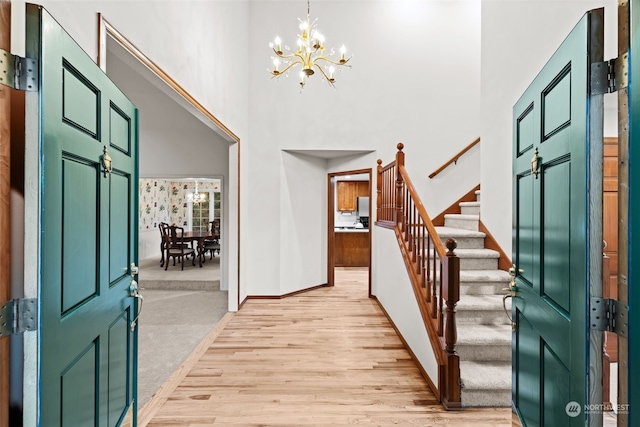 foyer featuring baseboards, a high ceiling, stairs, light wood-style floors, and a chandelier