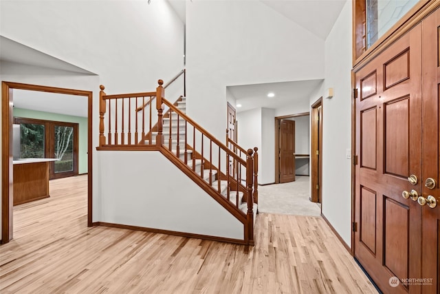 foyer entrance featuring light wood-type flooring, baseboards, stairs, and high vaulted ceiling